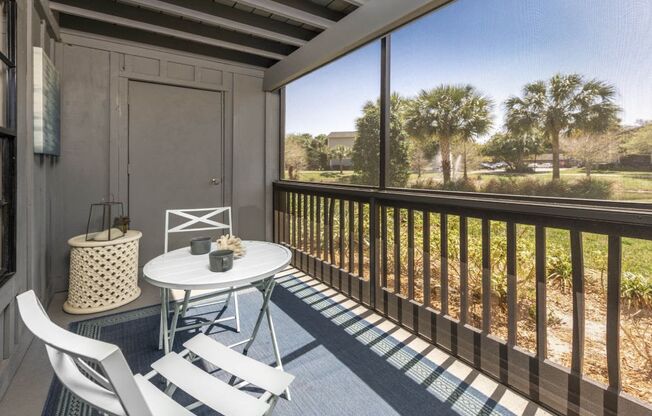 A balcony with a table and chairs overlooking a grassy area.