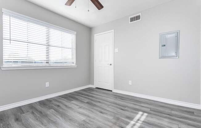 A room with a white door, a window with blinds, and a ceiling fan.