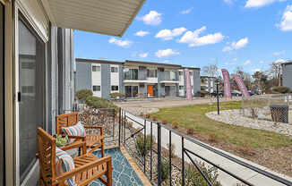 A balcony with two chairs and a table overlooks a grassy area with buildings in the background.