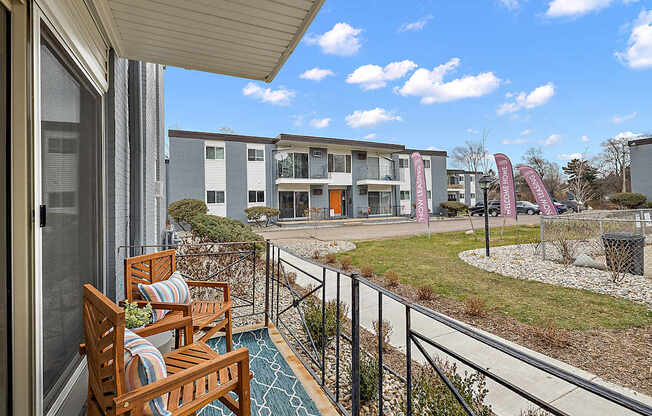 A balcony with two chairs and a table overlooks a grassy area with buildings in the background.
