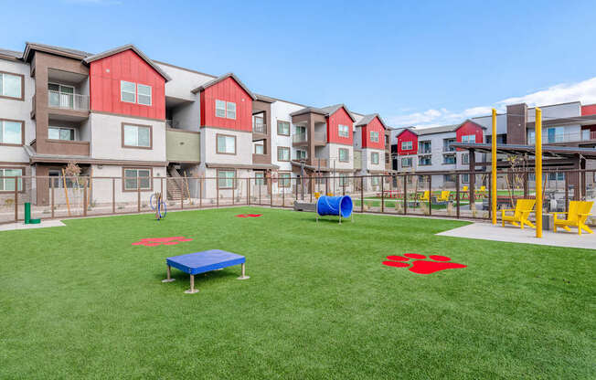 A playground area with a blue mat and red star on the grass in front of apartment buildings.