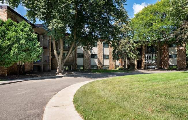 A tree-lined street in front of a brick building. White Bear Lake, MN White Bear Terrace Apartments