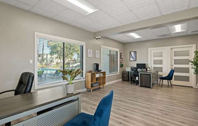 A room with a desk, chairs, and a window overlooking a parking lot.