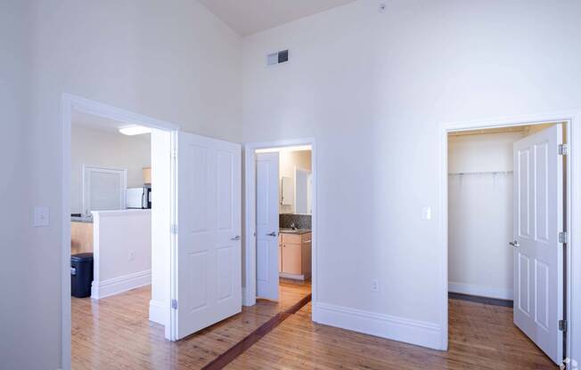 a living room with white walls and a wood floor and a kitchen