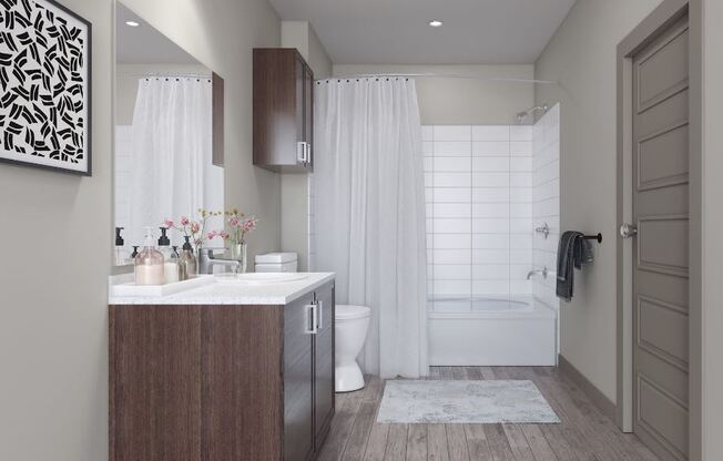 Modern bathroom here at 49 West Apartments with dark wood cabinets, large mirror, and white counter. Floral decor on the counter. White shower curtain and subway tiles in the shower.