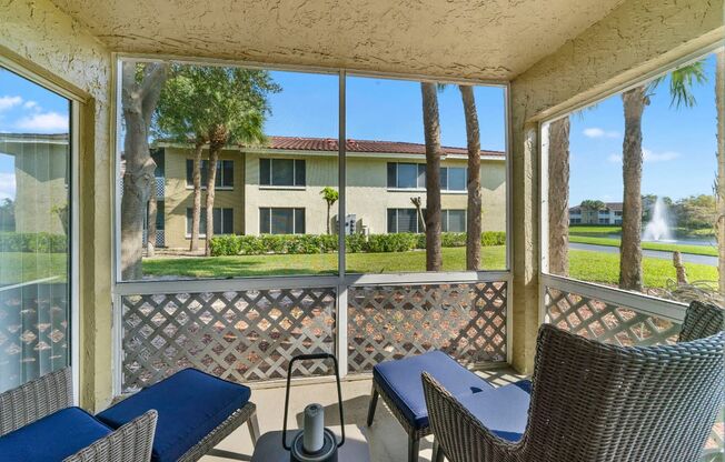 Patio with two chairs and table looking at exterior of aartment building and lake with fountain