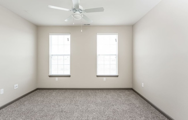 an empty room with a ceiling fan and two windows