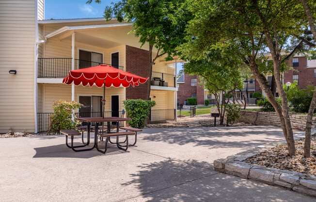 A red umbrella is on a table in the courtyard of a building.