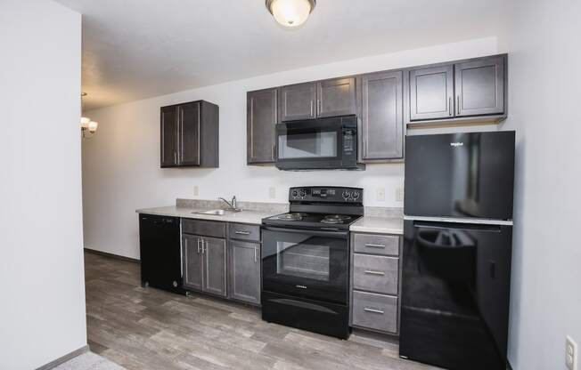 an apartment kitchen with black appliances and dark wood cabinets