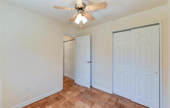 vacant bedroom with hardwood flooring, large closets, and ceiling fan at alpha house apartments in washington dc