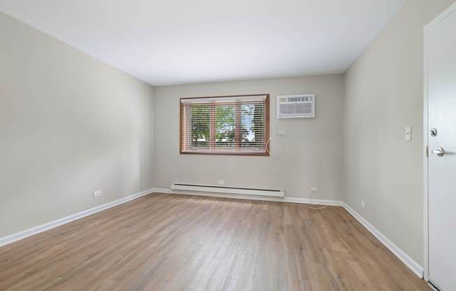 A room with wooden flooring and a window with blinds.