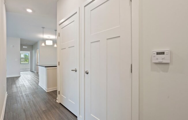 a white hallway with white closets and a kitchen