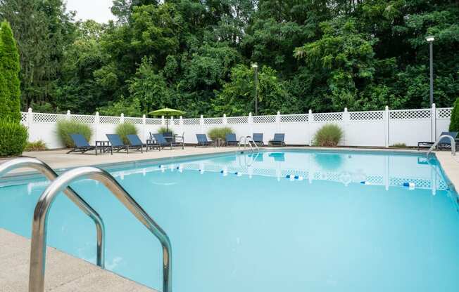 Two BR Apartments in Reynoldsburg, OH - The Oaks - Large Pool with Lounge Chairs and Patio Furniture Surrounded By Lush Large Green Trees