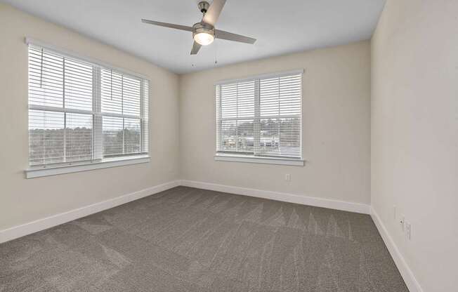 A room with a ceiling fan and two windows.