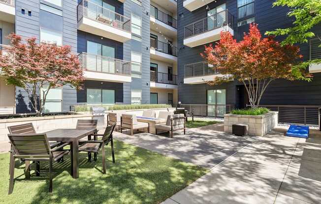An outdoor courtyard area with a table and chairs is surrounded by apartment buildings at Knox Heights Apartments in Dallas, TX