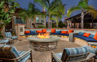 A fire pit in the middle of a patio surrounded by chairs and cushions.