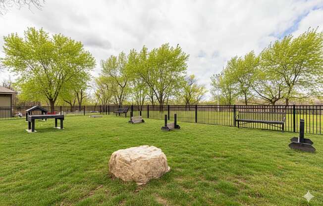 A park with a large rock in the middle of a grassy area.