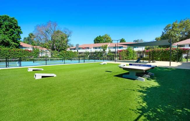 a picnic table and ping pong table sit in the middle of a grassy area at The Park Apartments, California