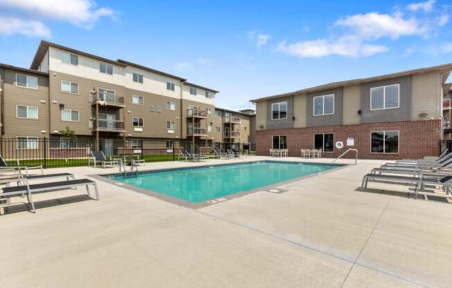 A swimming pool is surrounded by sun loungers in front of apartment buildings.