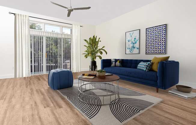 Apartments in Dallas, TX - Trend Design District - Living Room with Faux-Wood Flooring, Area Rug, Sofa, Ottoman, Round Coffee Table, Wall Art, Houseplant, Ceiling Fan, and Sliding Glass Door.