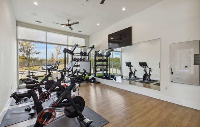 a home gym with various exercise bikes and a television on the wall at LynnCora, Grand Prairie, Texas