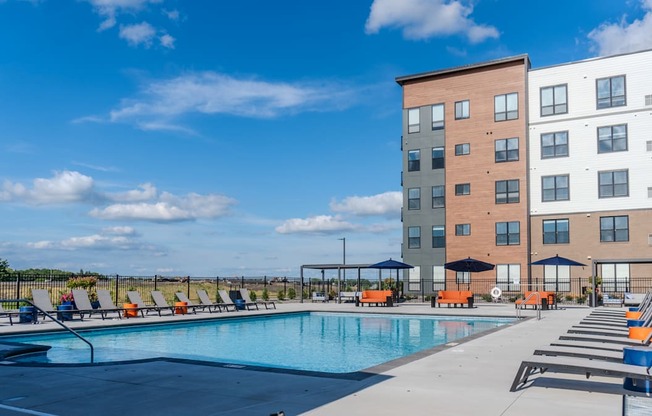 A swimming pool surrounded by orange lounge chairs and apartment buildings.