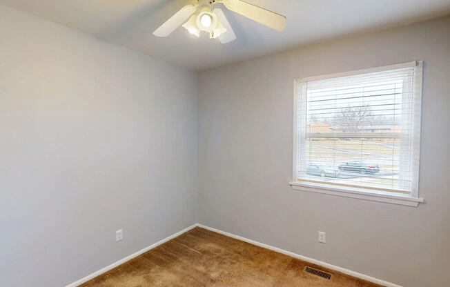 A room with a ceiling fan and a window with blinds.