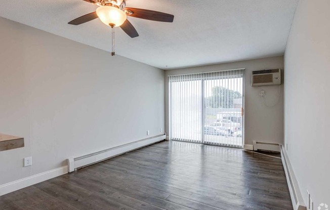 an empty living room with a large window and a ceiling fan