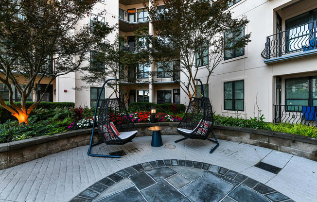 a courtyard with two swing chairs and a small table in front of an apartment building