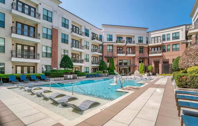 A large swimming pool surrounded by lounge chairs and apartment buildings.
