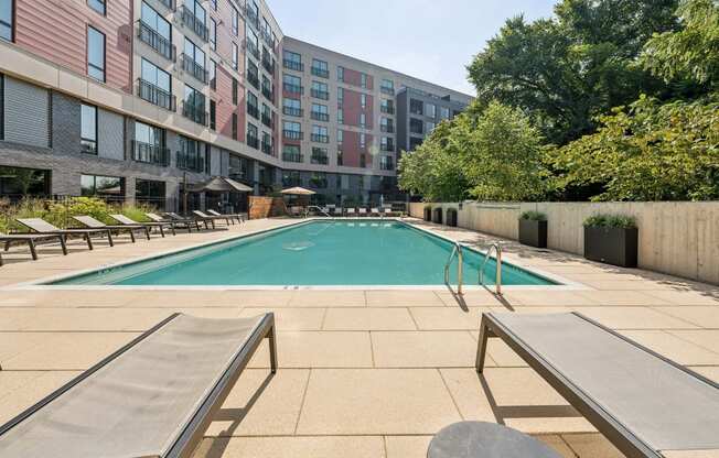 A pool surrounded by sun loungers and a building in the background.