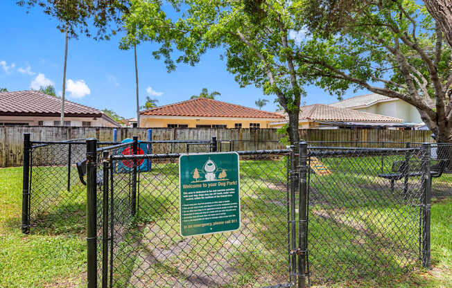 A sign welcoming visitors to a dog park is displayed on a fence.