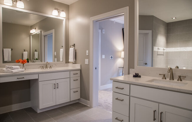 Master bathroom with two vanities, a neutral colored wall, and white cabinets in the penthouse