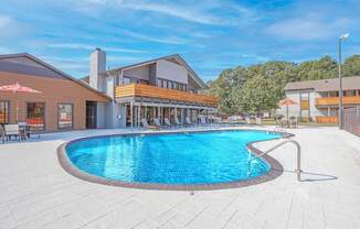 A large outdoor swimming pool surrounded by a patio area with lounge chairs and umbrellas at The Marq apartments in Shreveport, LA