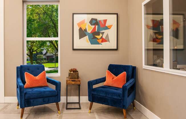 two blue chairs with orange pillows in a room with two windows