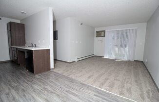 an empty living room with a kitchen in the background