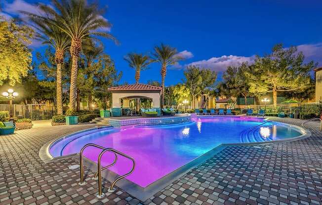 a large swimming pool at night with palm trees at Mirasol Apartments, Las Vegas