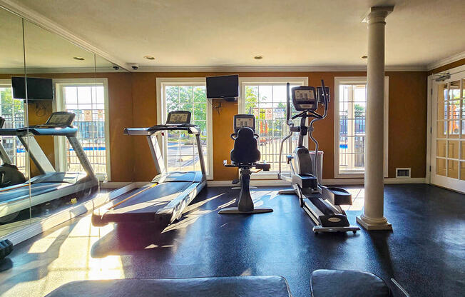 a gym with cardio equipment in a large room with windows