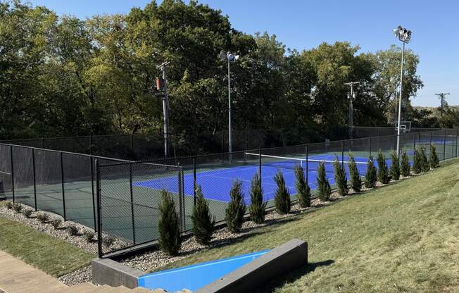 a tennis court with a fence around it and a blue pool at The Boulevard, Roeland Park, KS