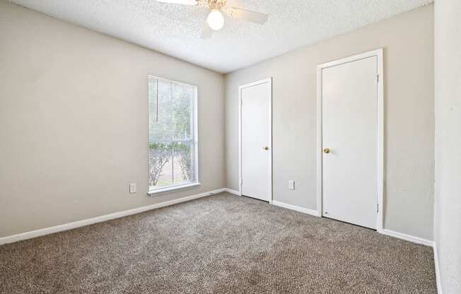 A room with a carpeted floor, a ceiling fan, and three doors.