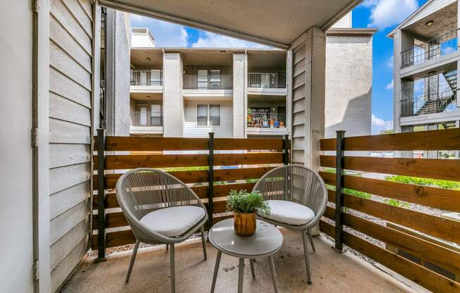 a patio with two chairs and a table in front of a fence