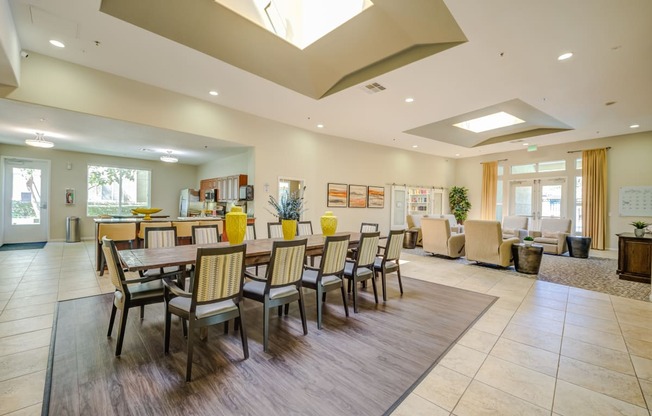 a resident clubhouse with a long table with chairs and a kitchenette in the background