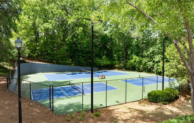 A tennis court surrounded by trees and a lamp post.