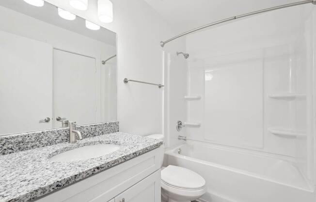 A bathroom with a granite countertop and a white tub and shower