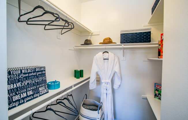 a walk in closet with a white robe and shoes and a shelf with hangers