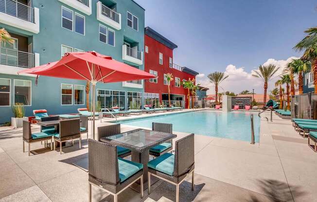 A pool area with a table and chairs and a red umbrella.