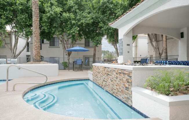 A small pool with a stone wall and a white building in the background.