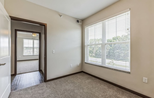 an empty living room with a large window and a door to a hallway