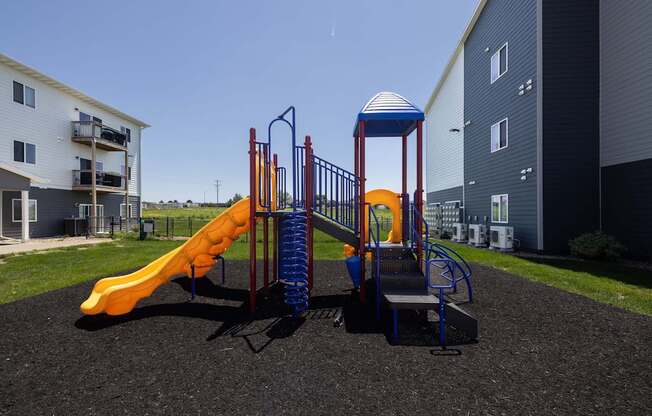A playground with a yellow slide and a blue and red structure.
