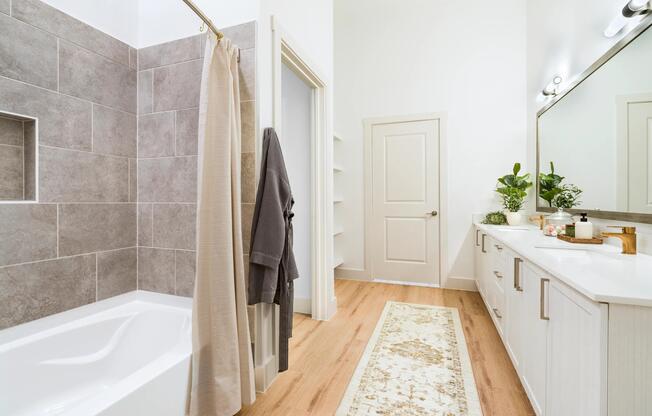 Primary bathroom with a tiled soaking tub, extended vanity, and warm wood style flooring designed for everyday comfort and easy routines.